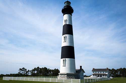 The Bodie Island Lighthouse standing tall against the blue sky.